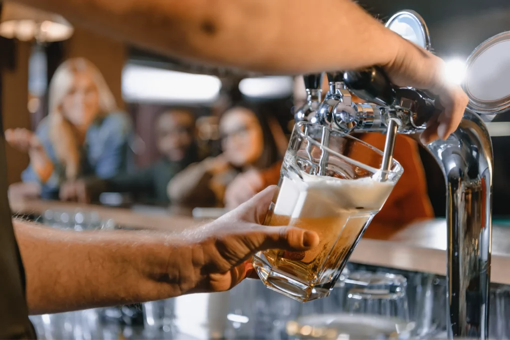 Bartender pouring beer into glass from tap at a local brewhouse for guest on craft beer tour booked with acx travel.