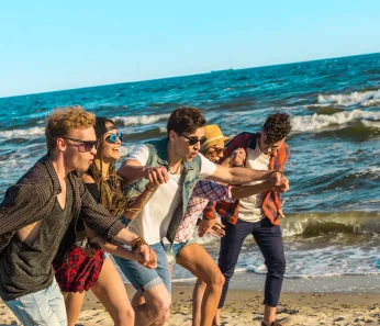 Happy friends running on the beach that booked their trip with acx travel.
